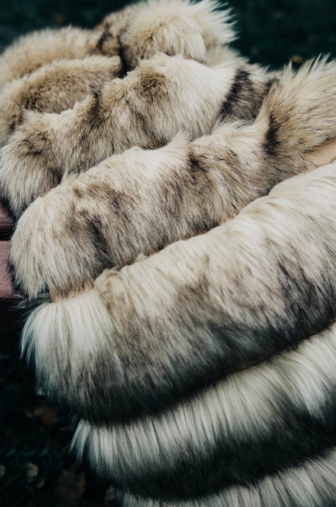 Kremowe futro z długim włosem, ułożone warstwami na drewnianej powierzchni, z delikatnym cieniowaniem i widoczną fakturą włosia. Ciepłe, naturalne odcienie.