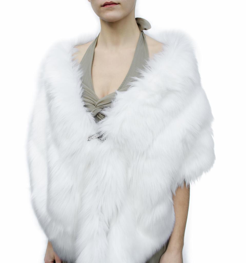 Modelka prezentuje białe futrzane bolerko z ozdobną broszką w kształcie skrzydeł, założone na sukienkę z dekoltem halter.