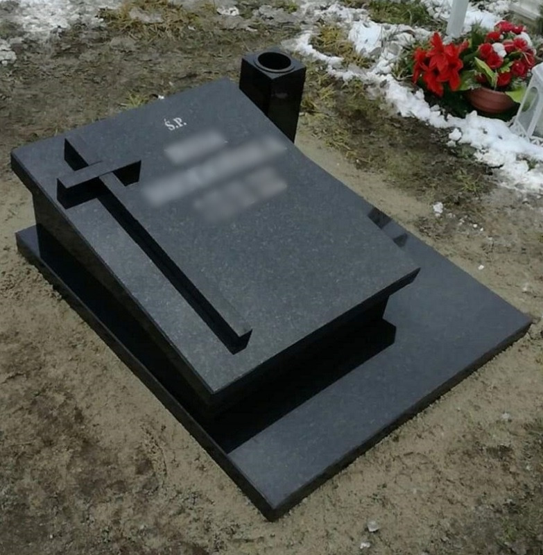 Czarny, granitowy pomnik z krzyżem, wazonem i kwiatami na cmentarzu, częściowo pokrytym śniegiem.