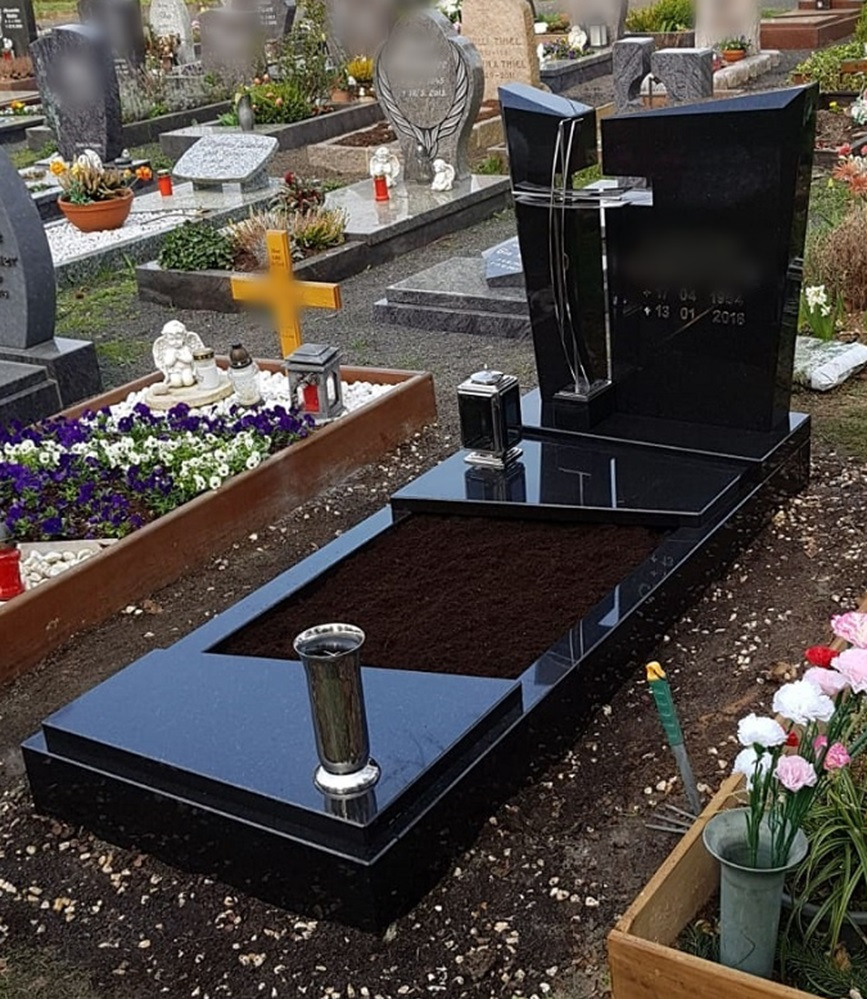 Czarny, polerowany pomnik z przezroczystym krzyżem na cmentarzu, otoczony innymi grobami i kwiatami, z widoczną datą urodzin i śmierci.