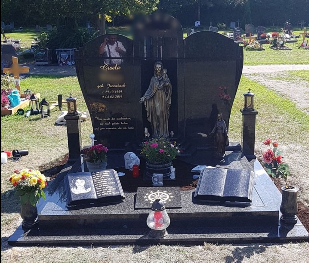 Czarny, polerowany pomnik nagrobny z rzeźbą Madonny z Dzieciątkiem, dwoma otwartymi księgami z wygrawerowanymi portretami, oraz wizerunkiem osoby rozmawiającej przez telefon umieszczonym...