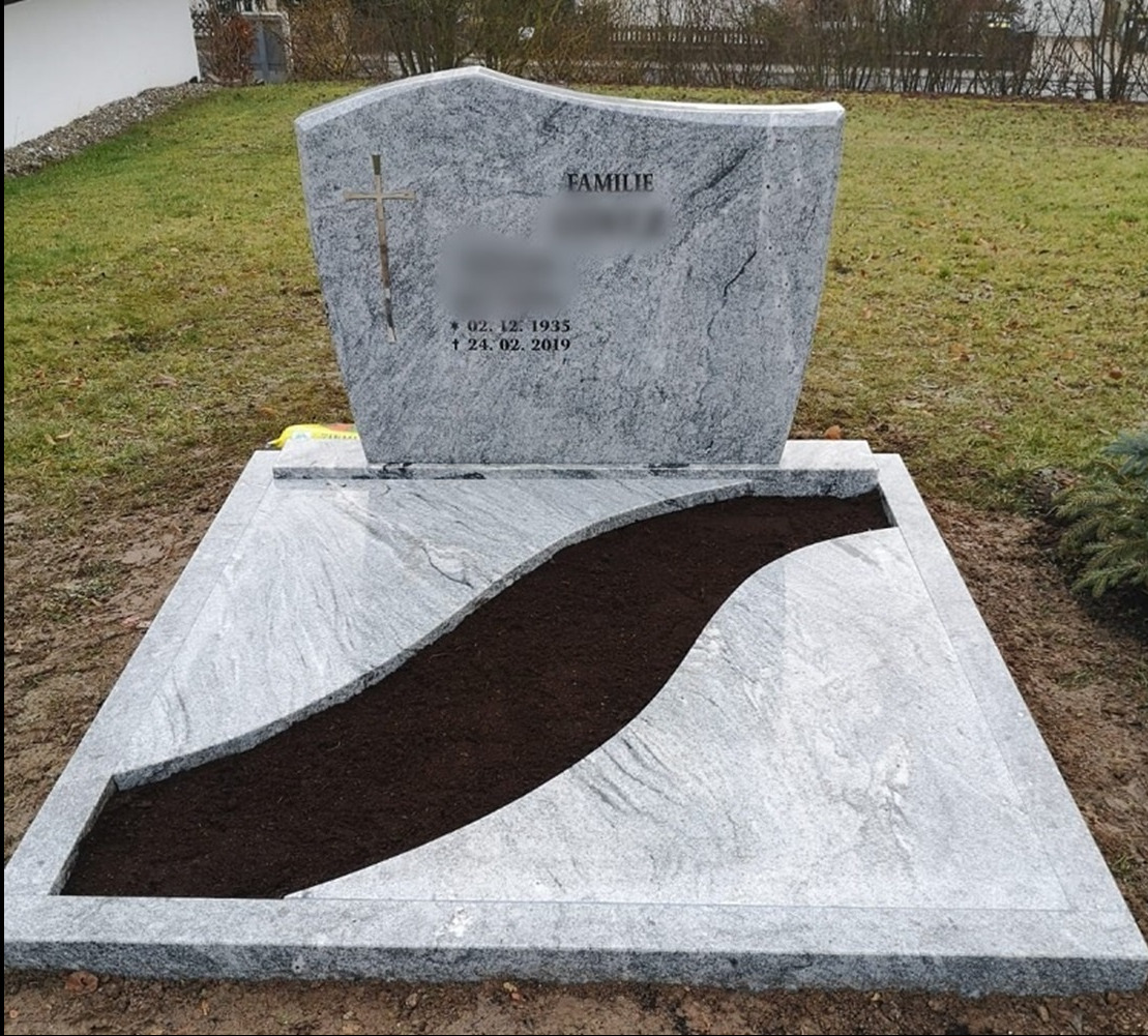 Jasnoszary, granitowy pomnik z wygrawerowanym krzyżem i napisem 'Familie', daty urodzin i śmierci, z miejscem na ziemię w kształcie fali, na cmentarzu.