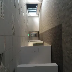 Wnętrze biurowca z widokiem na sufit z oknem dachowym, ściany wykończone płytami z widocznymi otworami wentylacyjnymi i szarą teksturowaną tapetą.