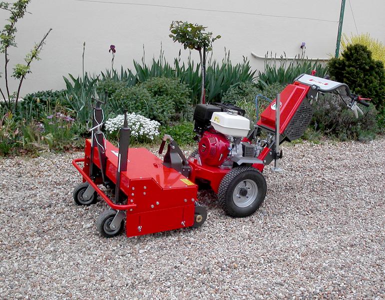 Czerwona aeracja trawnika, maszyna z silnikiem Honda na żwirowym podłożu, tło z zielenią i ścianą. Sprzęt do pielęgnacji trawników w ogrodzie.