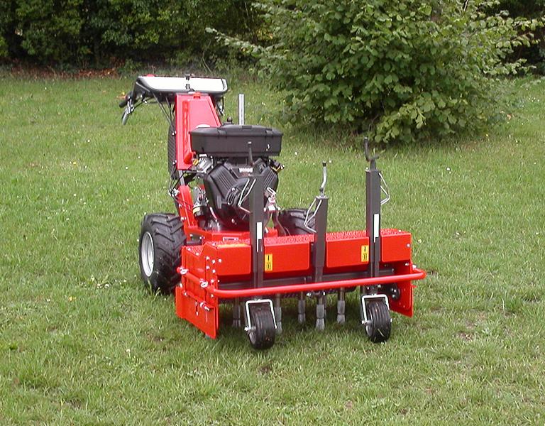 Aerator spalinowy w kolorze czerwonym na trawniku, widok z tyłu, z elementami roboczymi w kontakcie z podłożem. Maszyna do pielęgnacji trawników.