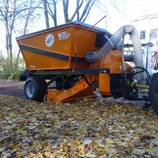 Pomarańczowa maszyna Votex VT420 do zbierania liści na traktorze, z rurą ssącą i zbiornikiem, na tle drzew i opadłych liści.