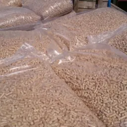 Foliowe worki wypełnione jasnymi, drewnianymi granulkami, prawdopodobnie gotowe do transportu, ułożone w stos na nieokreślonym podłożu.