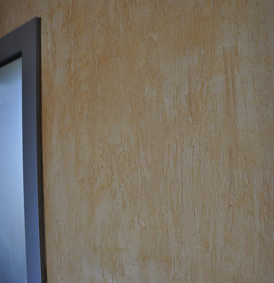 Beżowa ściana z fakturą w Czeladzi, imitująca naturalne drewno, widoczny fragment ościeżnicy drzwiowej.