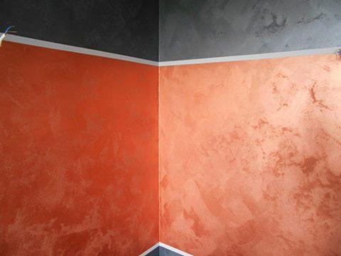 Pomarańczowo-brązowa ściana z efektem dekoracyjnym w rogu pomieszczenia, górna część ściany pomalowana na szaro, biała listwa sufitowa.