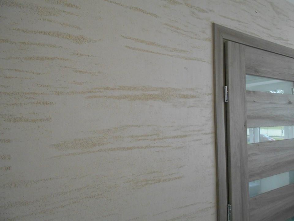 Ściana z efektem dekoracyjnym trawertynu w odcieniach beżu, sąsiadująca z drewnianą ościeżnicą i drzwiami z przeszkleniami.