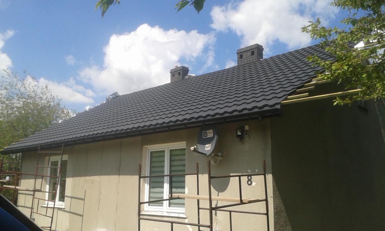 Nowy, grafitowy dach z blachodachówki na domu w Rudzie-Hucie, widoczne kominy z cegły oraz fragment rusztowania.