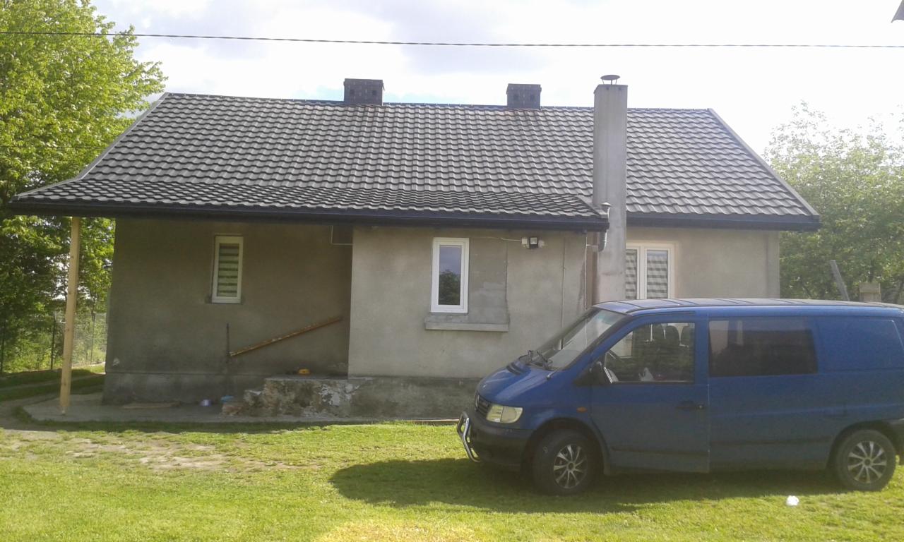 Dom jednorodzinny z szarą dachówką, widoczny komin i zaparkowany niebieski bus.