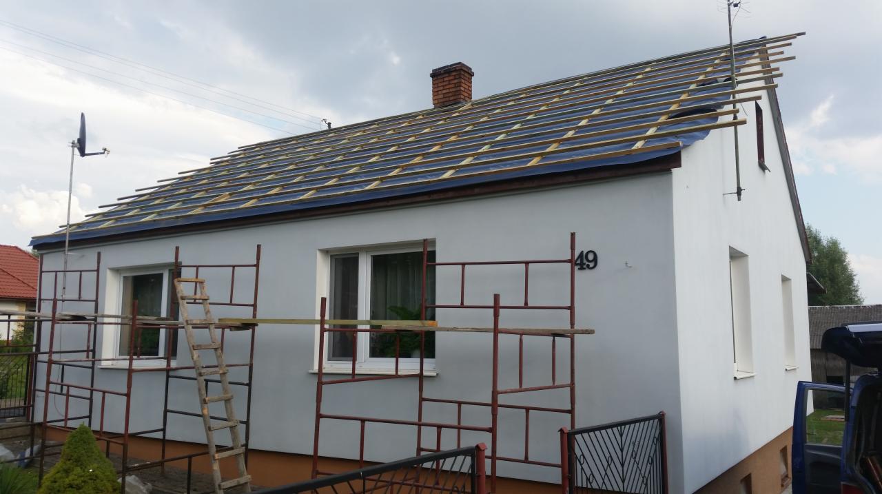 Dom jednorodzinny w trakcie krycia dachu, widoczne łaty pod pokrycie, rusztowania przy ścianie, numer posesji 49.
