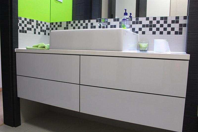 Nowoczesna łazienka z białą, prostokątną umywalką nablatową i szafką pod umywalką z czterema frontami, wzbogacona o czarno-białą mozaikę na ścianie i zielony akcent kolorystyczny w postaci ręcznika...