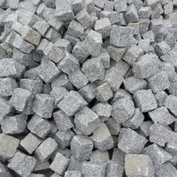 Stos szarych, surowych kostek o nieregularnych kształtach, z widoczną fakturą granitu, ułożonych w chaotyczny sposób.