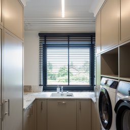 Architekt Wnętrz Wojtaś Patrycja - Nowoczesna pralnia w beżowych odcieniach: zabudowa meblowa, marmurowy blat z umywalką przy oknie z żaluzjami, pralka i suszarka. Minimalistyczny design, eleganckie wykończenie.