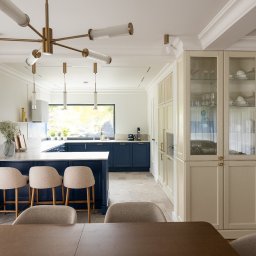 Architekt Wnętrz Wojtaś Patrycja - Elegancka kuchnia w bieli i granacie: wyspa z hokerami, przeszklona witryna, designerska lampa. Stonowana kolorystyka i dbałość o detale tworzą spójną całość.