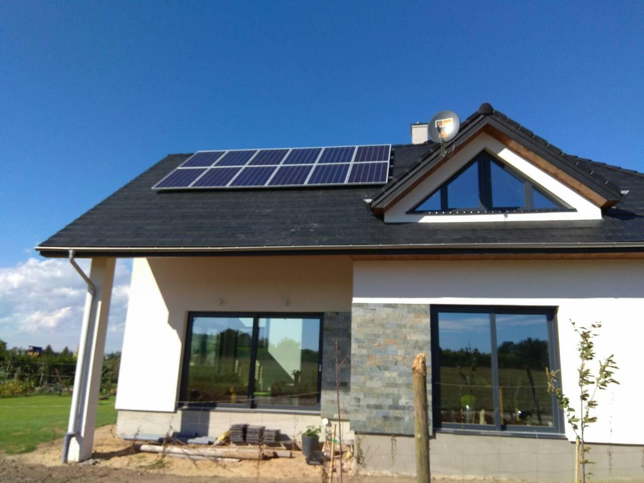 Dom jednorodzinny z panelami fotowoltaicznymi na dachu, widok z zewnątrz w słoneczny dzień. Nowoczesna architektura z elementami kamiennej elewacji.