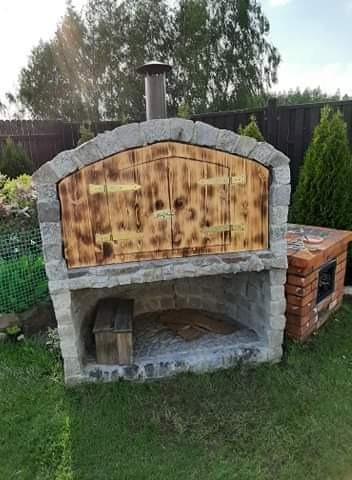 Ogród z murowanym piecem chlebowym z drewnianymi drzwiczkami i kominem, obok mała wędzarnia z cegły
