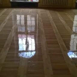 Błyszcząca, świeżo polakierowana parkietowa podłoga w jasnych odcieniach drewna z wyraźnym odbiciem okna, po renowacji.