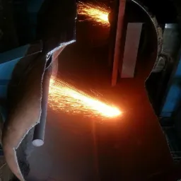 Cięcie metalowej konstrukcji palnikiem; iskry i płomienie oświetlają wnętrze konstrukcji z widocznymi elementami wsporczymi i śladami cięcia.