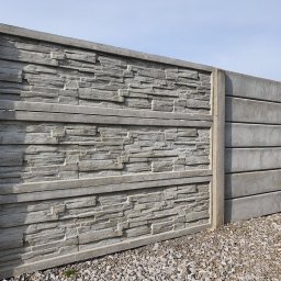 PROFIKS Ogrodzenia - Szary, betonowy płot z prefabrykatów o fakturze imitującej kamień łupany, widoczny na tle nieba i żwirowego podłoża.