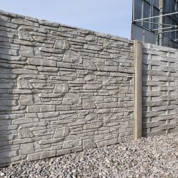 PROFIKS Ogrodzenia - Dwa panele ogrodzeniowe z betonu: jeden imitujący kamień, drugi z wzorem plecionki, oddzielone słupem, na tle żwirowego podłoża i metalowej konstrukcji.