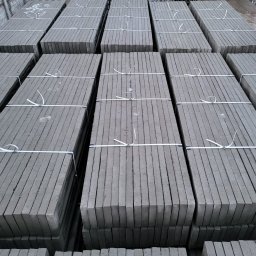 PROFIKS Ogrodzenia - Szare płyty betonowe ułożone w stosy i zabezpieczone białymi taśmami, widoczne rowki na krawędziach płyt.