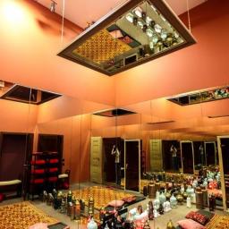 Oles Project Sp. Z o.o. - Pomieszczenie z pomarańczowymi ścianami, wyposażone w lustra, orientalne dywany, poduszki i dekoracyjne lampiony, z lustrzanym sufitem podwieszanym na łańcuchach.