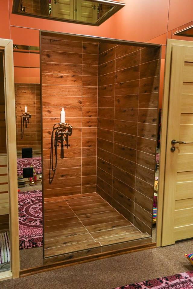 Kabina prysznicowa wyłożona brązowymi płytkami imitującymi drewno, z zamontowaną baterią w stylu retro i widocznym odbiciem wnętrza w lustrzanej ścianie.