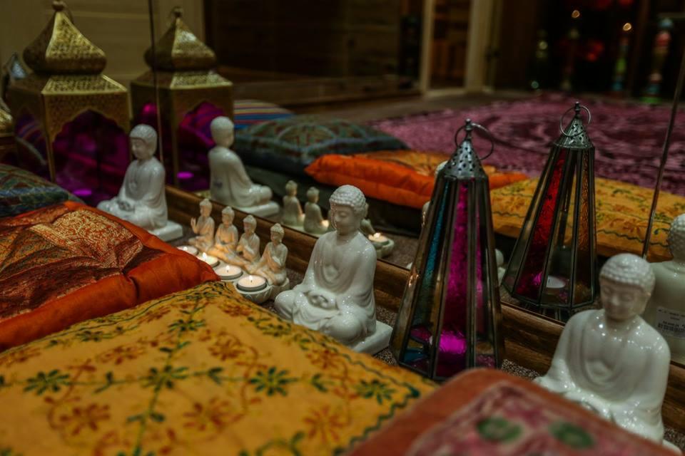 Aranżacja wnętrza z poduszkami w orientalne wzory, ceramicznymi figurkami Buddy, świecami i lampionami z kolorowymi szybkami, odbijająca się w lustrze