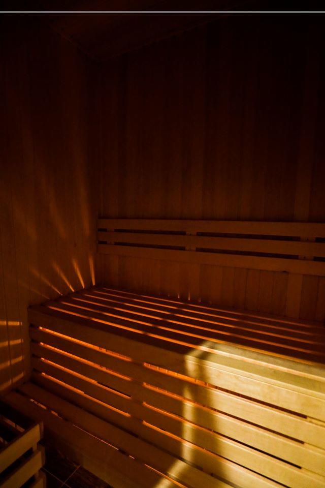 Wnętrze sauny z drewnianymi ławkami, oświetlone ciepłym światłem tworzącym wyraźne cienie na ścianach.