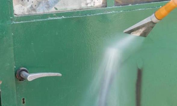 Zielone drzwi z metalową klamką czyszczone parownicą pod ciśnieniem, widoczne ślady wcześniejszych zabrudzeń i odchodzącej farby.