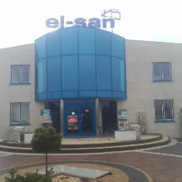 Budynek biurowy z elewacją z jasnych płyt, duże okna i przeszklenia w kolorze niebieskim, logo firmy na dachu, wyeksponowane materiały elewacyjne na zewnątrz.