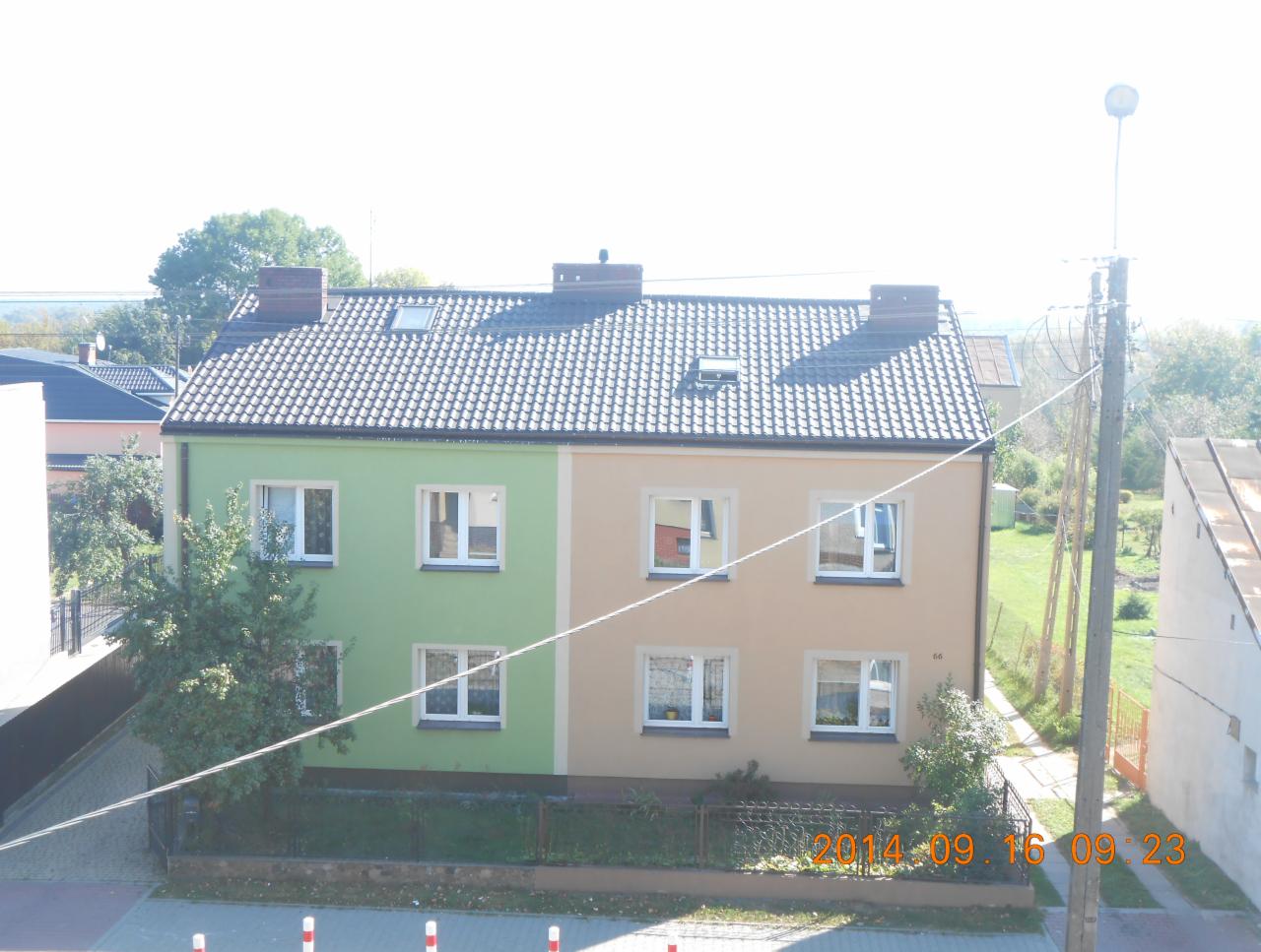 Dwukondygnacyjny dom z dachem pokrytym szarą dachówką, widoczne okna dachowe i kominy, budynek pomalowany na zielono i beżowo, sfotografowany z góry.