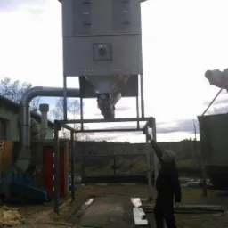 Szara, przemysłowa instalacja z metalu, prawdopodobnie system filtracji powietrza, w trakcie montażu na zewnątrz budynku, widoczna osoba wskazująca na górną część konstrukcji.