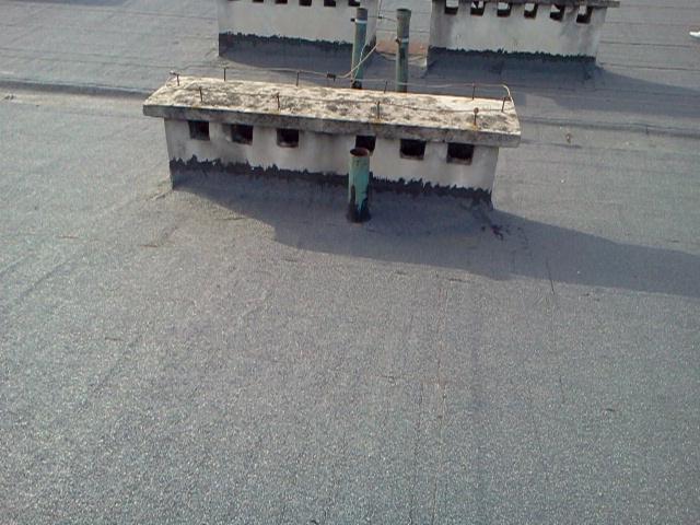 Szczegółowe ujęcie płaskiego dachu pokrytego papą, z widocznymi kominami wentylacyjnymi i elementami konstrukcyjnymi. Widok z góry.