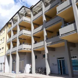 Wielopiętrowy budynek z balkonami po odświeżeniu elewacji, widoczny pracownik przy schodach, rowery zaparkowane obok.