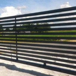 Nowoczesna brama posesyjna z poziomych, metalowych profili w kolorze grafitowym, widok z zewnątrz, z zielonym tłem w oddali i fragmentem ogrodzenia po lewej.