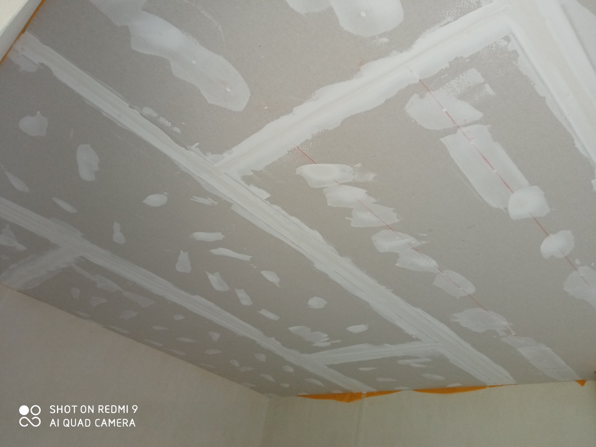 Sufit z płyt kartonowo-gipsowych, na którym widoczne są miejsca łączeń i wkrętów po szpachlowaniu, z widocznymi liniami pomocniczymi wyznaczonymi czerwoną nicią.