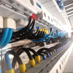 Szczegółowe ujęcie pod kątem na listwę zaciskową w rozdzielnicy elektrycznej z uporządkowanymi kablami w kolorach niebieskim i czarnym z końcówkami w kolorach żółtym, niebieskim i szarym...