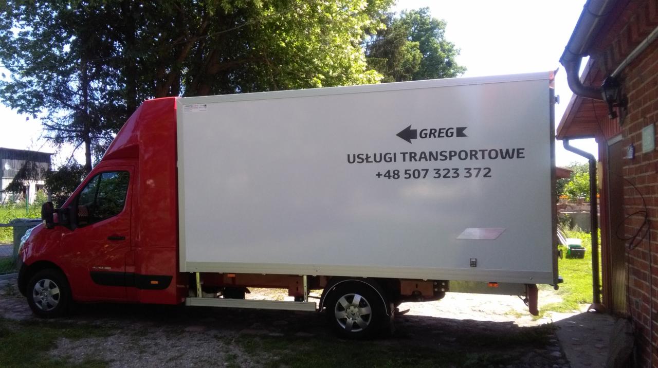 Czerwony bus transportowy z białą zabudową, z logo firmy 'Greg' i numerem telefonu, zaparkowany obok ceglanego budynku w słoneczny dzień.