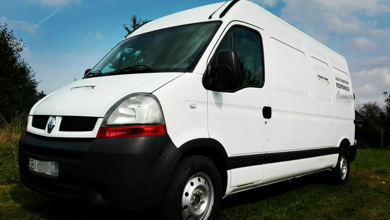 Biały bus Renault Master na trawiastym podłożu z widocznymi napisami 'Usługi Transportowe' i 'Przeprowadzki' na boku, z lekko pochmurnym niebem w tle.