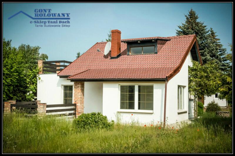 Dom jednorodzinny z czerwonym dachem z dachówki, antena satelitarna na kominie. Widok z poziomu trawy.