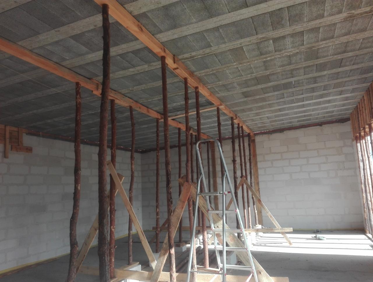 Wnętrze budynku w trakcie budowy z widocznym szalunkiem stropu podpartym drewnianymi stemplami i drabina aluminiowa w tle, ściany z betonu komórkowego.