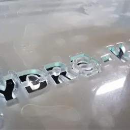 Proces wycinania liter 'HYDROMAX' w szkle za pomocą strumienia wody pod ciśnieniem, widoczne krople wody na powierzchni obrabianego materiału.