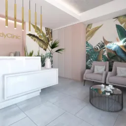 Nowoczesne wnętrze recepcji kliniki z białym biurkiem, złotymi lampami wiszącymi, ścianą z motywem tropikalnych liści i neonem, oraz strefą oczekiwania z fotelami i stolikiem kawowym.
