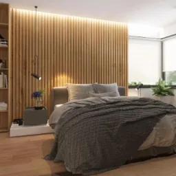 Nowoczesna sypialnia z drewnianą ścianą z lameli podświetloną od góry, drewniany regał z książkami i dekoracjami, łóżko z szarą narzutą, stolik nocny z kwiatami i lampką, rolety w oknach.