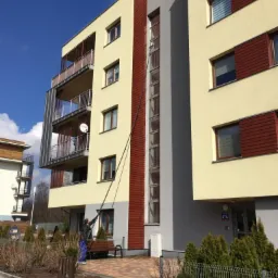 Czyszczenie okien na zewnątrz budynku wielorodzinnego za pomocą długiej lancy teleskopowej, widoczny pracownik w trakcie wykonywania usługi.