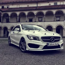 Elegancki, biały Mercedes CLA z dekoracjami ślubnymi na tle arkadowego dziedzińca. Tablica rejestracyjna z napisem 'Młoda Para'.